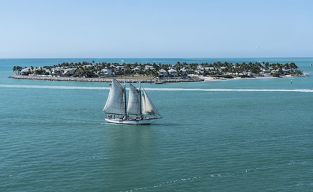A sailboat with full sails moves past an island in the Bahamas.のeditorial素材