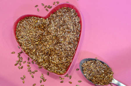 Flax seeds in the shape of a heart on a pink background, top view. Super food. Healthy vegan concept.の写真素材
