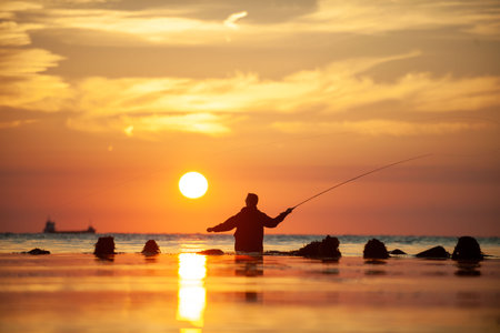 Silhouette of fisherman with fishing rod at sunset time on the beachの写真素材