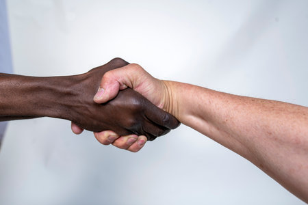 Arms of two anonymous men shaking hands with each other on a gray background. Two unrecognizable people of different ethnicities shaking hands.の写真素材