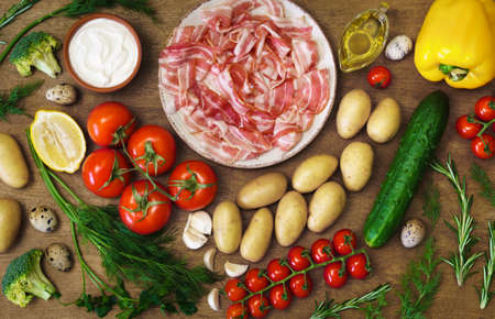 Countless summer vegetables, quail eggs and ham on the wooden rustic table. Concept of village menu, organic food.の写真素材