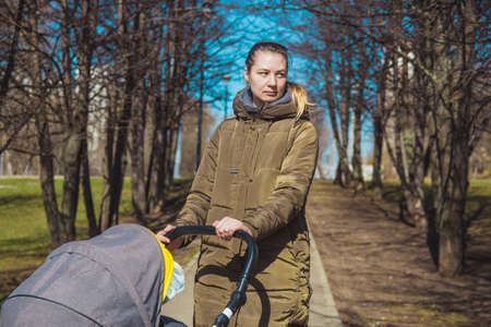 beautiful and young woman mother and baby in a stroller walking in the parkの写真素材
