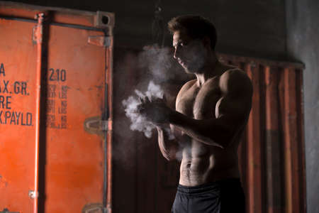 Athlete with a naked torso clapping rubs talc before performing the exercises. Studio shot.の写真素材