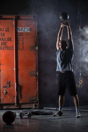Bald charismatic athlete doing kettlebell swings. Studio shot in a dark tone.の写真素材