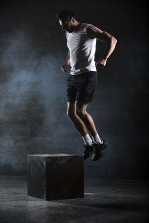 Athlete gave exercise. Jumping on the box. Phase touchdown. Studio shots in the dark tone.の写真素材