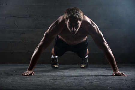 Athlete with a beautiful body and a naked torso doing push-ups exercise on the floor. Studio shot in...