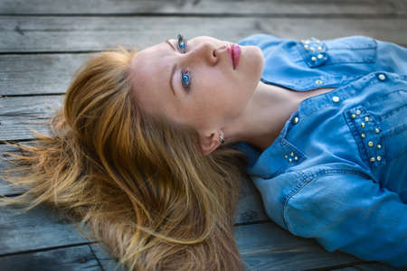 red-haired girl with bright blue eyes lying on a wooden pavement and looks at the sky. outdoor shooting.の写真素材