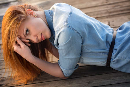 Red-haired girl with blue eyes lying on a wooden pavement and looks at the camera. Outdoor shooting.の写真素材