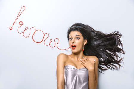 Admiration of a beautiful brunette girl. From the mouth of the red thread on a white background in the studio is written Wowの写真素材