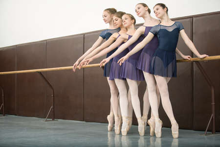 Five ballet dancers in class near the barre. Model wearing white tights. Girls look towardの写真素材