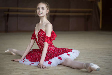 Ballerina sitting on the floor in the splits dressing in red tutu. Dancer is smiling.の写真素材