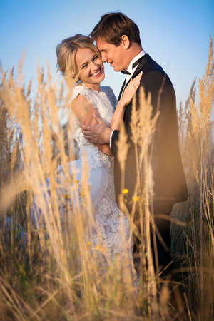 Young wedding couple standing in a field of pigweed in the setting sun. Newlyweds hug with a smile.の写真素材
