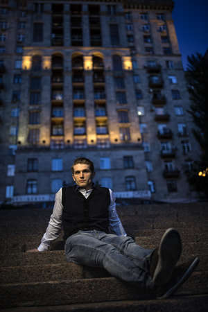 Handsome guy in a suit sitting on stairs against backdrop of the city building. Evening shot.の写真素材