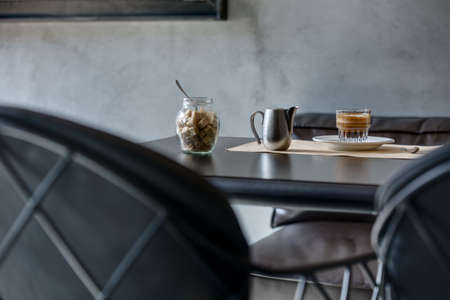 Espresso on black glossy table. Restaurant submission of coffee in a glass, milk in steel carafe and cane sugar in a glass jar.の写真素材