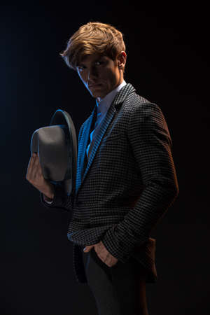 Redheaded man in a plaid suit with hat in hand on a black background in the studioの写真素材