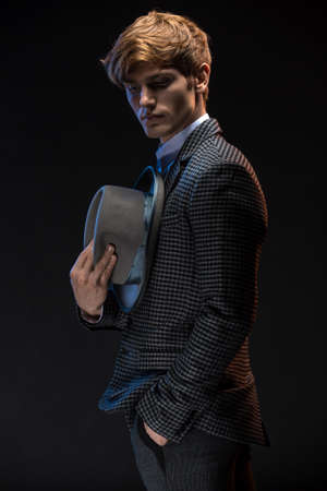 Redheaded man in a plaid suit with hat in hand on a black background in the studioの写真素材