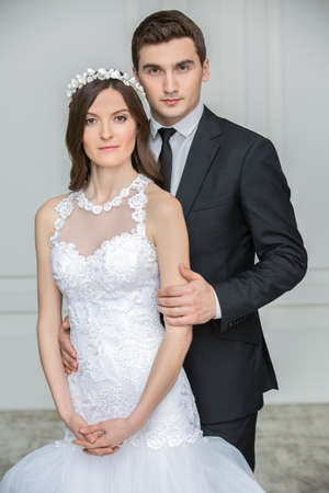 Beautiful fashion bridal couple. Studio shooting. The groom in a stylish black suit and the bride in a white dress with delicate decorative crown on his head.の写真素材