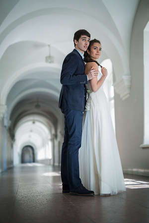 Newlywed couple near a window, groom sitting on the windowsill. The wife is next to him in a beautiful white dress.の写真素材