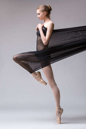 Slim dancer plays with black mesh fabric in the studio on a white background in lingerie.の写真素材