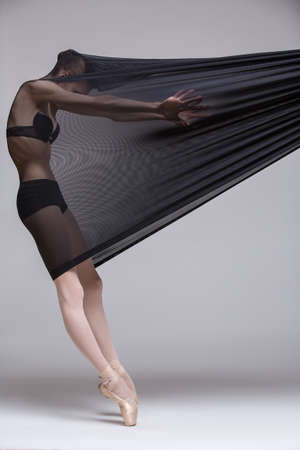 Slim dancer plays with black mesh fabric in the studio on a white background in lingerie.の写真素材