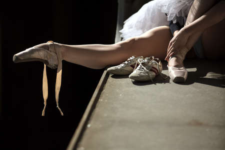 Ballerina sitting on the edge of the bridge. Feet shod with pointe. Dancer wearing a white tutu and blue swimsuit.の写真素材