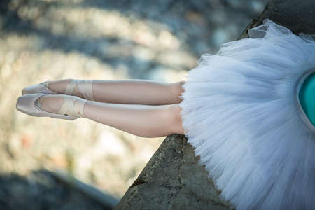 Ballerina sitting on the edge of the bridge. Feet shod with pointe. Dancer wearing a white tutu and blue swimsuit.の写真素材