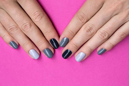 Delicate female hands with a stylish neutral manicure. Nail painted in different color gray nail polish. Against the backdrop of a bright purple background.の写真素材