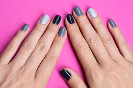 Delicate female hands with a stylish neutral manicure. Nail painted in different color gray nail polish. Against the backdrop of a bright purple background.の写真素材