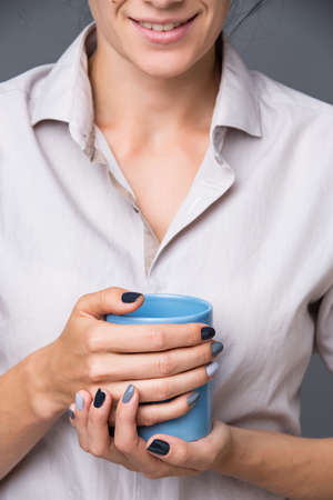 Beautiful well-groomed female hands with a stylish modern manicure holding a blue cup close-up. Each nails are made up of different shades of gray varnish. Face with smile.の写真素材