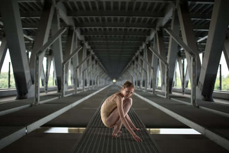 Portrait full height of young and graceful ballerina in a flesh-colored bathing suit, amid the urban landscape of the bridge.の写真素材