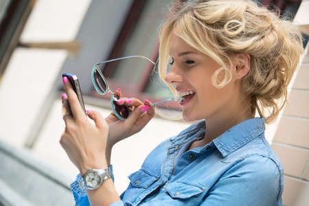 Closeup portrait of cute blonde in sunglasses and a bright blue denim shirt emotionally talking on a...