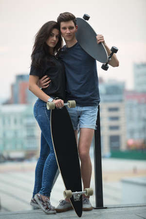 Pair of lovers teen is posing for the camera in an embrace with two longboard. Against the background of the urban landscape.の写真素材