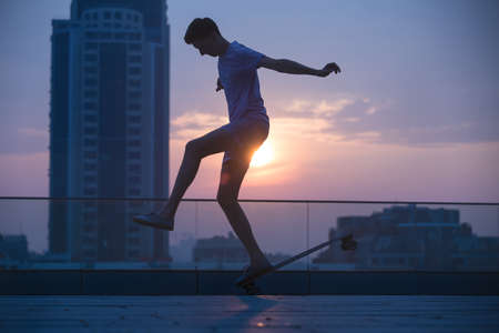 Stylish teenager makes a jump on a longboard tricks on urban city background sunset.の写真素材