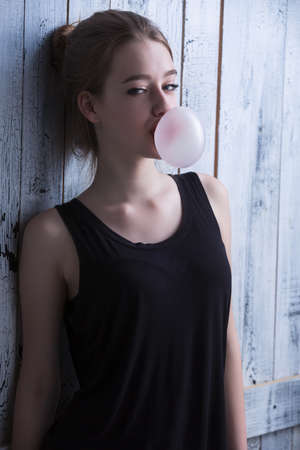 Portrait of sexual brown-haired, which inflates languidly pink bubble of chewing gum. Photographed...