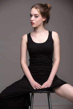 Blonde woman in sexy black dress sitting on a chair with your feet wide.の写真素材