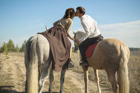 Romantic couple riding on two horses to drag each other for a gentle kissの写真素材