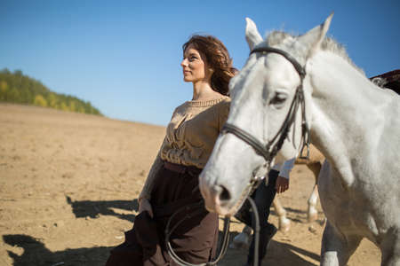 Beautiful girl is walking with white horse in a field in profile to the camera.の写真素材