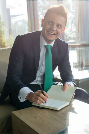Business man in a stylish suit with a beautiful smile, looking at sobessednik sitting at a table in the lounge. In his hand was a pen and note pad.の写真素材