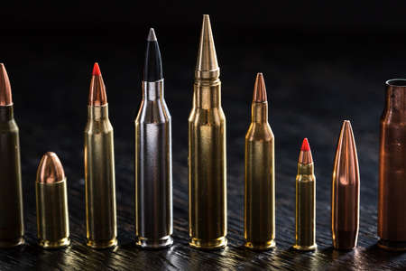 Number of large-caliber ammunition of different caliber in one line on a dark textural wooden background. Studio shot.の写真素材