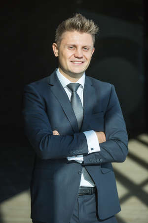 Portrait of stylish businessman in a nice suit near a large window. The man crossed his arms and looking at the camera.の写真素材