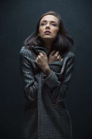 Brown-haired beautiful girl wrapped in a gray coat in a cage with her hair. Photographed in the...