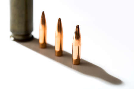 Macro shot of bullet casings on a white studio background. Sleeve casts a shadow on the tough end of which is shiny copper bullet.の写真素材