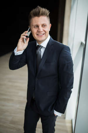 Man in a suit standing near window and talking on the phone.の写真素材