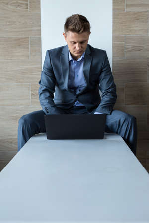 Blonde business man in a dark suit sitting on a bench at a laptop.の写真素材
