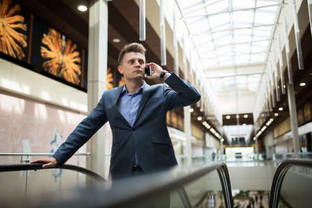 Business man in a dark suit talking on the phone on an escalator in the mallの写真素材