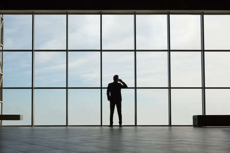Business man in a suit talking on the phone at a huge windowの写真素材