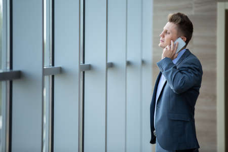 Business man in a suit talking on the phone looking at the windowの写真素材