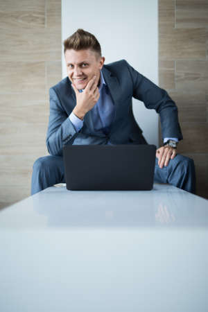 Business man in a suit with a laptop smiling. He sits on the benchの写真素材