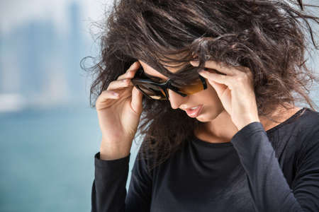 Girl with lush hair in a black dress on a background of sea and skyscrapers in Dubai. Beautiful...