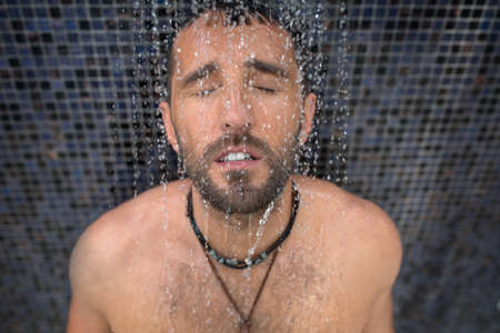 Winsome tanned dark-haired man with a naked torso in the shower. Tropical. Horizontal photoの写真素材